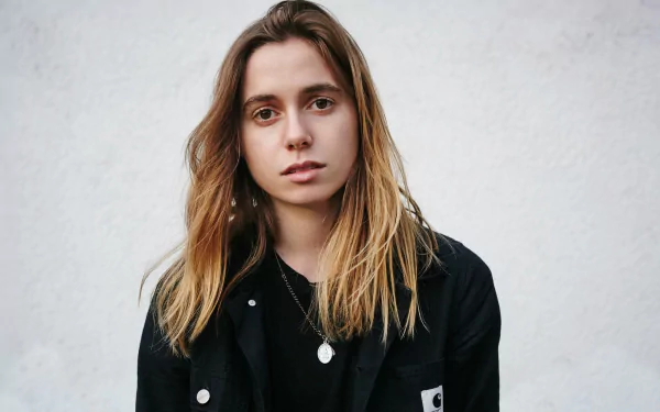 HD wallpaper featuring a portrait of a person with shoulder-length hair in a black jacket against a textured grey background.