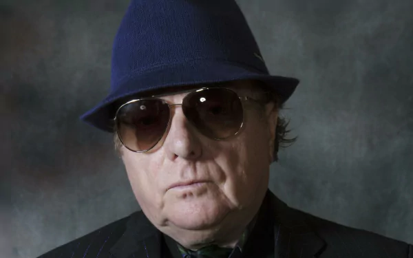 HD wallpaper featuring a moody portrait of a man in a blue fedora and sunglasses against a textured gray background.
