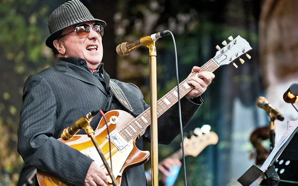 HD desktop wallpaper featuring a singer-songwriter performing on stage with a guitar in front of a microphone stand, providing a vibrant and inspiring musical background.