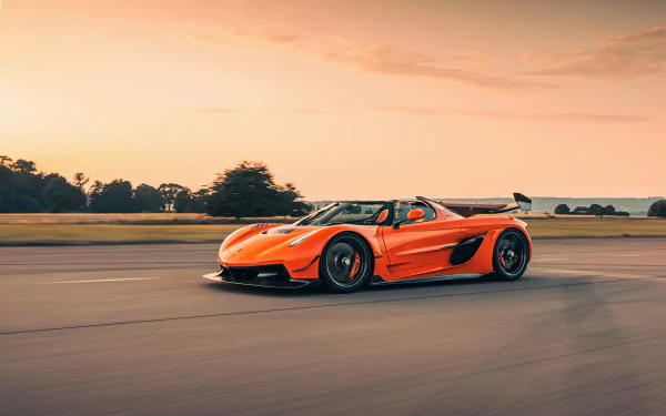 A vibrant orange Koenigsegg Jesko supercar speeds along a road at sunset, captured in stunning 8K Ultra HD for a sleek PC desktop wallpaper.