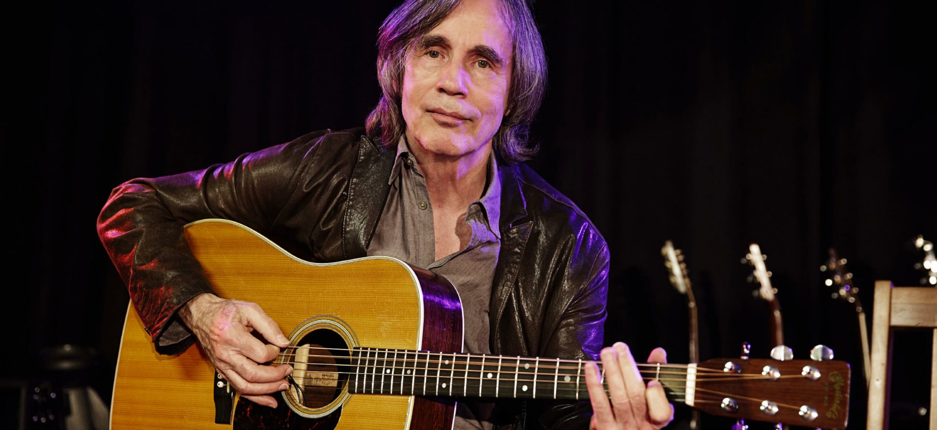 A high-definition desktop wallpaper featuring Jackson Browne, a renowned musician, holding his guitar while performing on stage, exuding a warm, inviting atmosphere.