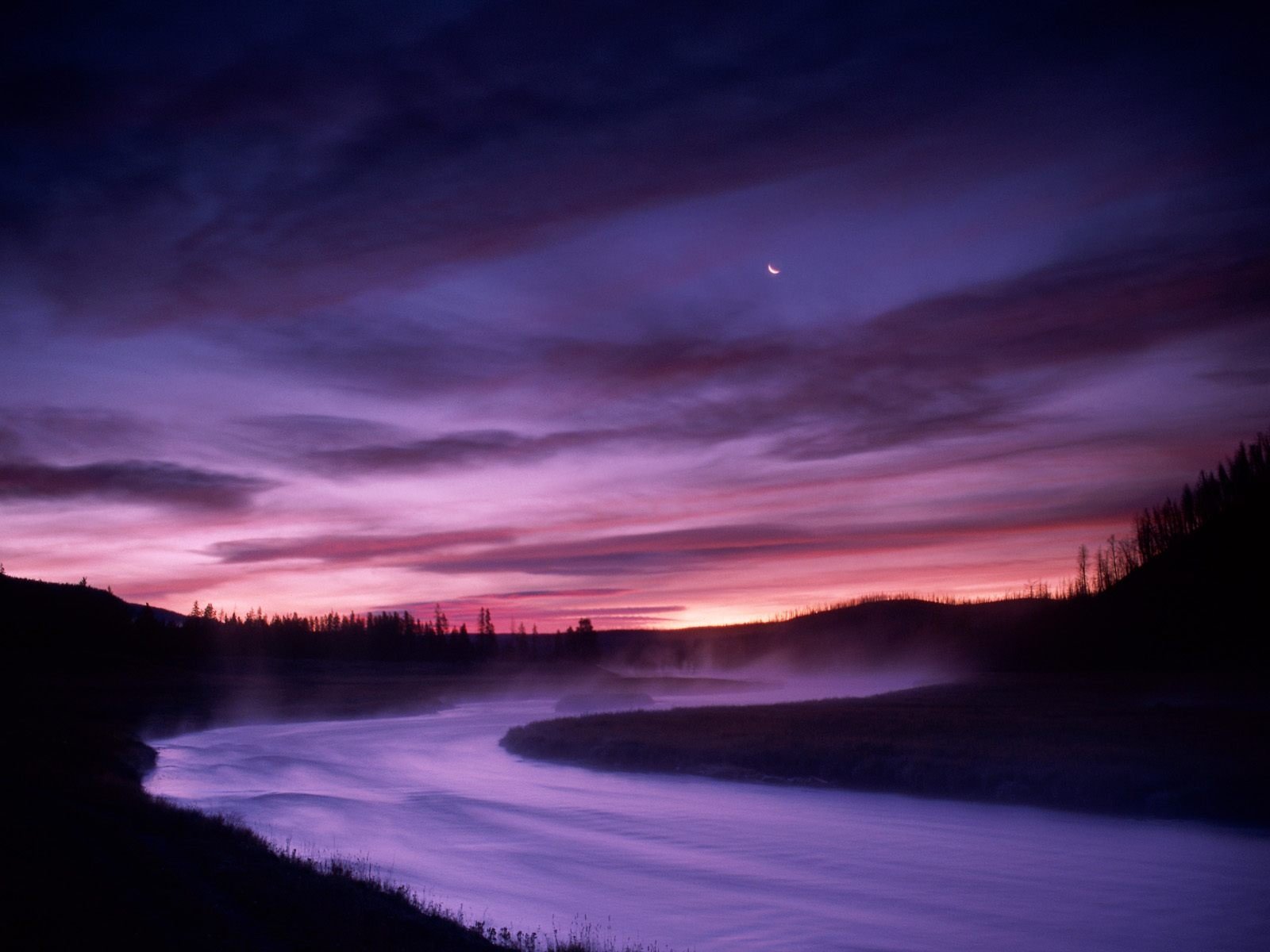 A serene river winds through a tranquil landscape, bathed in the soft hues of a twilight sky. This stunning nature scene makes a captivating HD desktop wallpaper.