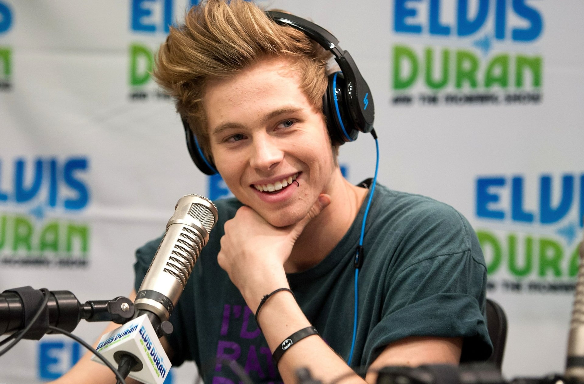 Smiling young man with headphones speaking into a microphone for a HD desktop wallpaper background.