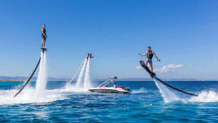 A dynamic flyboard scene captures athletes soaring above the water, powered by jets, with a boat in the background, showcasing the thrill of water sports in this vibrant HD wallpaper.