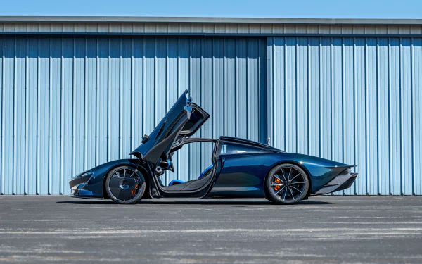 Side profile of a metallic blue McLaren Speedtail supercar vehicle with dihedral doors open, parked before a corrugated hangar — 4K Ultra HD PC desktop wallpaper and background