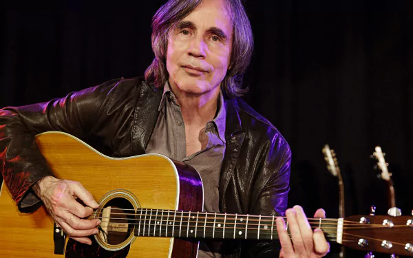 A high-definition desktop wallpaper featuring Jackson Browne, a renowned musician, holding his guitar while performing on stage, exuding a warm, inviting atmosphere.