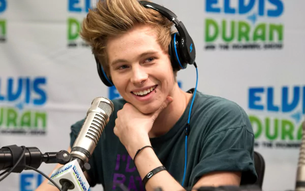 Smiling young man with headphones speaking into a microphone for a HD desktop wallpaper background.