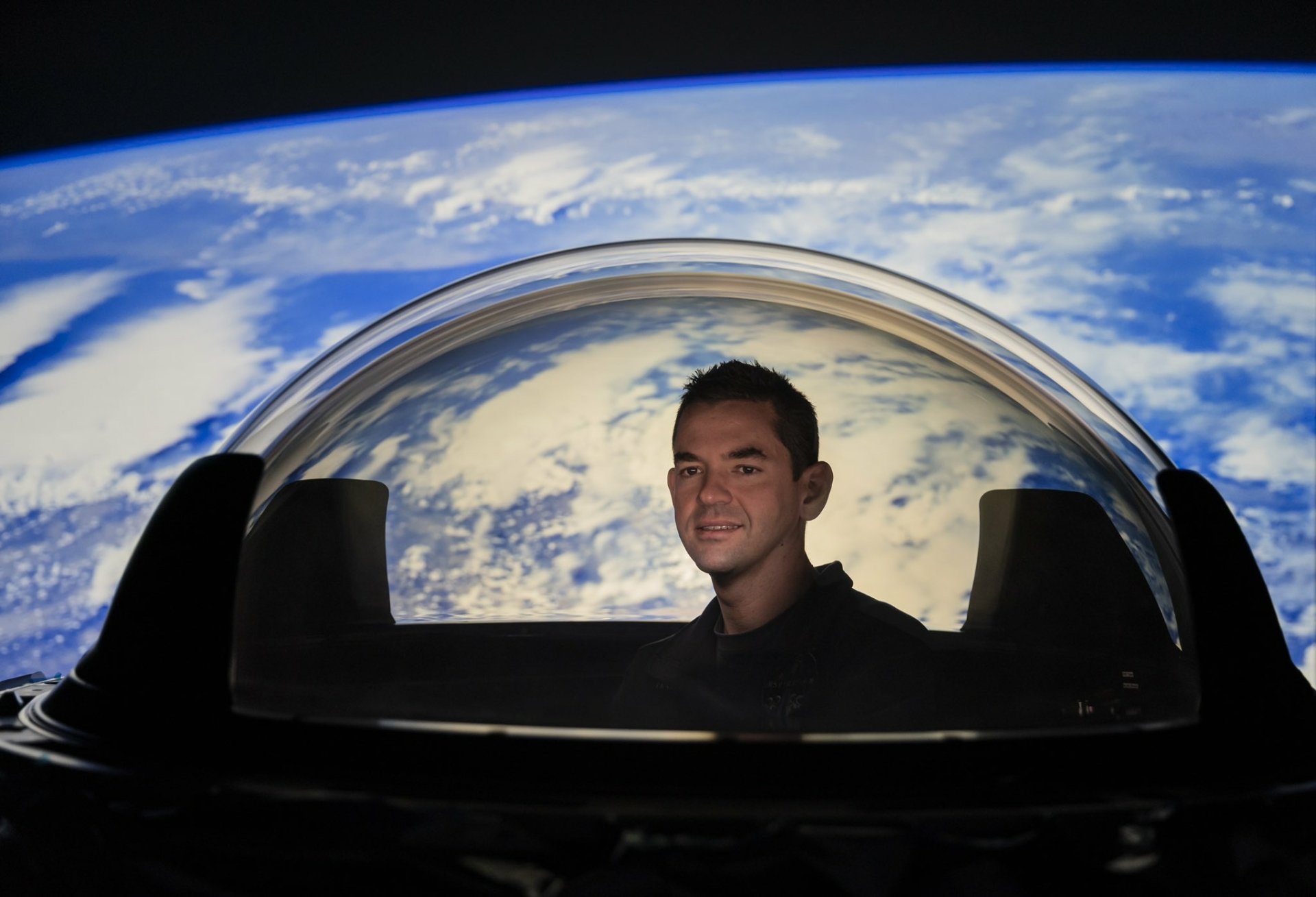 Person smiling inside Inspiration4 spacecraft with stunning view of Earth from space as HD desktop wallpaper background.