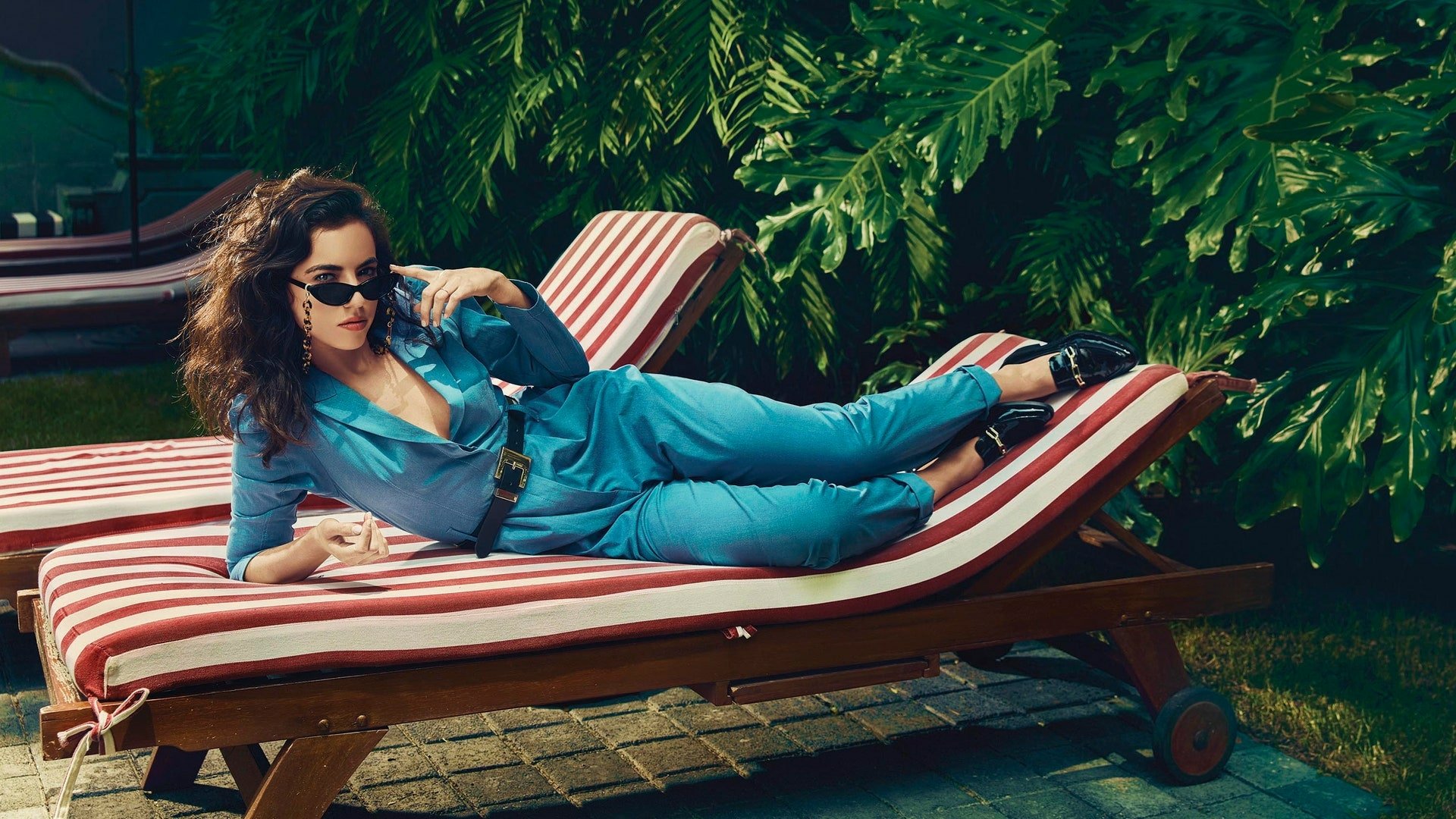 Cristina Rodlo lounges on a striped chaise in a vibrant blue outfit, surrounded by lush greenery, creating an eye-catching HD desktop wallpaper and background.