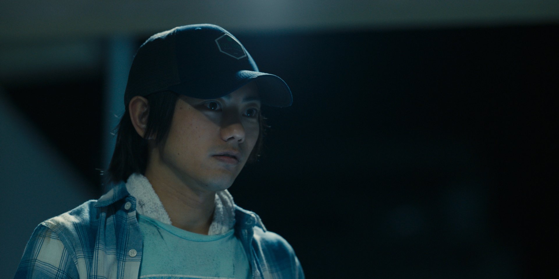 Moody close-up of a young man in a cap and plaid shirt under blue lighting — Alice in Borderland TV show 2K Quad HD PC desktop wallpaper and background.