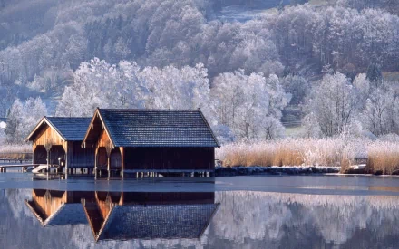 HD desktop wallpaper showing a serene winter landscape with wooden boathouses on a calm lake, surrounded by frost-covered trees in a natural setting.