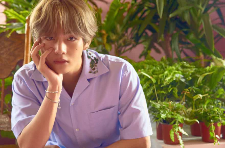 4K Ultra HD wallpaper of V (Kim Taehyung) from BTS, a K-pop singer, posing thoughtfully amidst lush green plants.