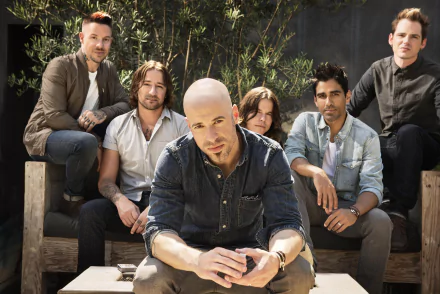 HD wallpaper featuring a group of musicians posing casually outdoors, with a prominent individual seated at the forefront.