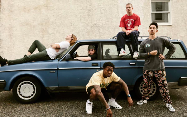 HD wallpaper of five people casually posed with an old blue car, presenting a relaxed and stylish vibe for a desktop background.