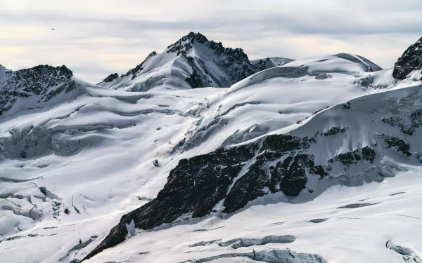 Snow-covered mountain peaks under a cloudy sky, showcasing natural beauty in a 4K Ultra HD snow and nature landscape.