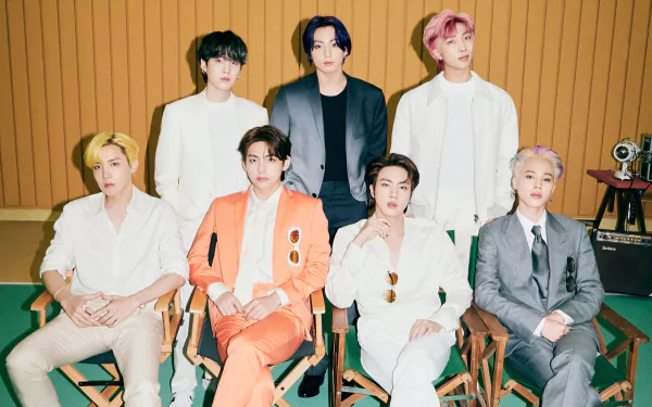 HD PC desktop wallpaper featuring the seven BTS members—RM, Suga, Jin, J-Hope, Jimin, V, and Jungkook—posing together in stylish outfits against a warm wooden backdrop.