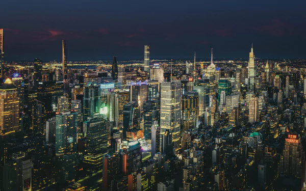 8K Ultra HD PC desktop wallpaper/background: nighttime aerial view of New York City skyline with illuminated skyscrapers and other man-made buildings.