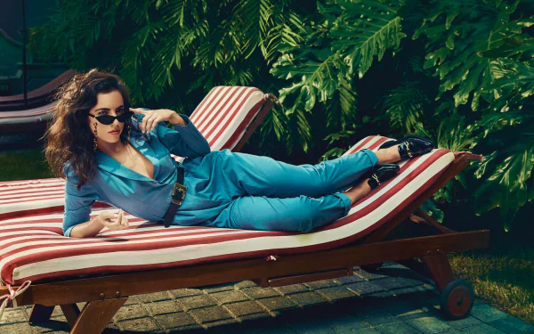 Cristina Rodlo lounges on a striped chaise in a vibrant blue outfit, surrounded by lush greenery, creating an eye-catching HD desktop wallpaper and background.