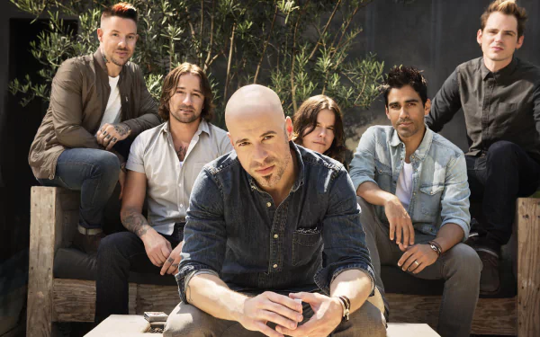 HD wallpaper featuring a group of musicians posing casually outdoors, with a prominent individual seated at the forefront.