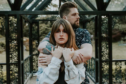 HD wallpaper featuring two individuals in a warm embrace, standing in a black gazebo with a natural backdrop, tagged with Spiritbox.