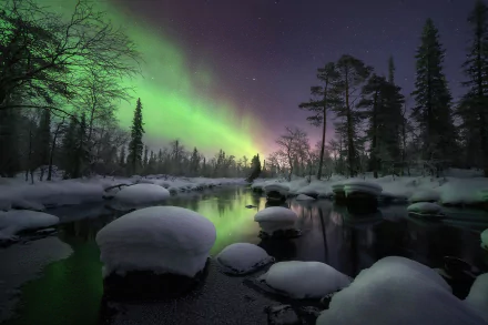 A serene winter night landscape with snow-covered rocks by a river, illuminated by the vibrant green aurora borealis in the dark sky, captured in HD for a desktop wallpaper.