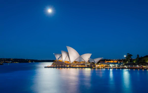 Moonlit, iconic man-made Sydney Opera House illuminated at night, its sails reflecting on calm harbor waters — 4K Ultra HD PC desktop wallpaper.