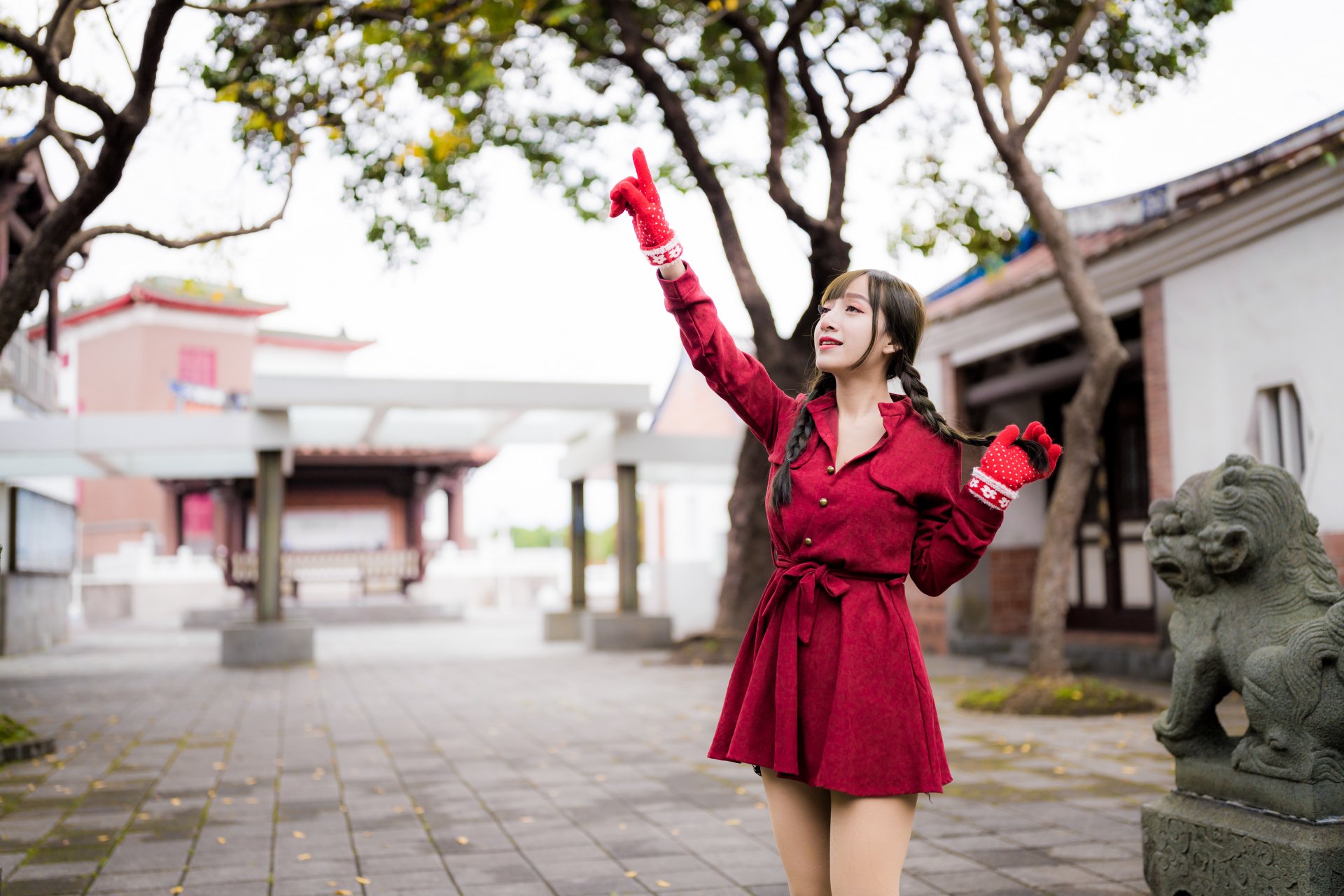 Asian woman with braided hair wearing a red dress and gloves poses outdoors near traditional architecture, captured in 4K Ultra HD for PC wallpaper.