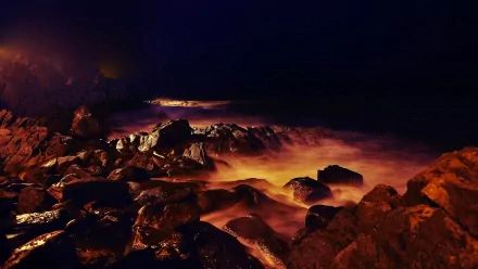 HD desktop wallpaper showcasing Spain's island coast at night, featuring rugged beach rocks and softly illuminated waves in a striking natural landscape.