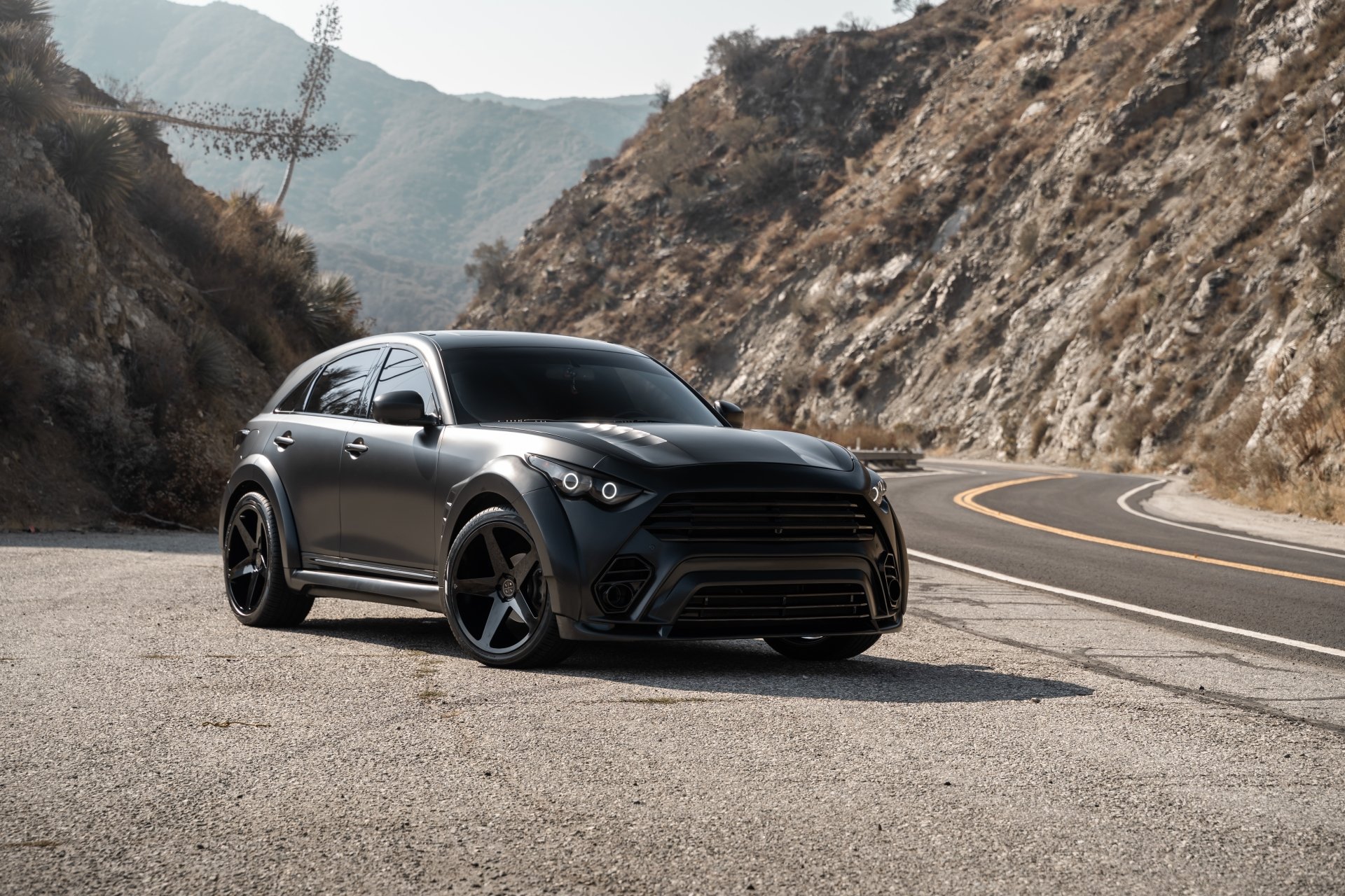 Matte black Infiniti QX70 SUV vehicle parked on a winding mountain road — 5K Ultra HD PC desktop wallpaper background.