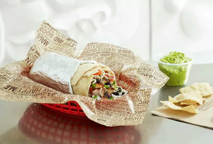 A visually appealing HD desktop wallpaper featuring a delicious burrito wrapped in paper, accompanied by a cup of guacamole and tortilla chips on a stylish surface.