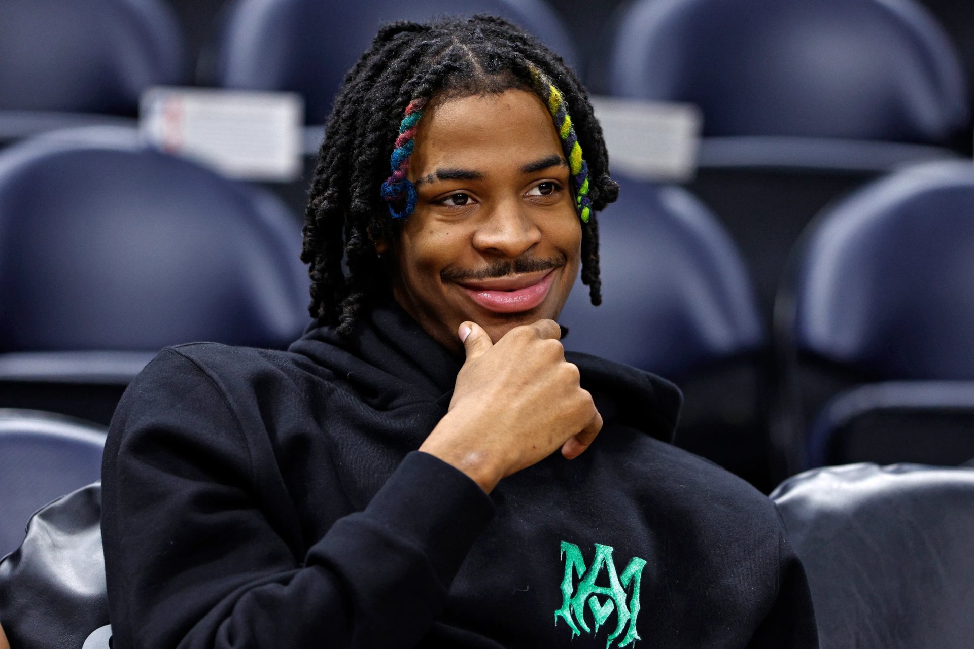 HD PC desktop wallpaper featuring basketball player Ja Morant with colorful braided hair, smiling and seated in a sports arena.