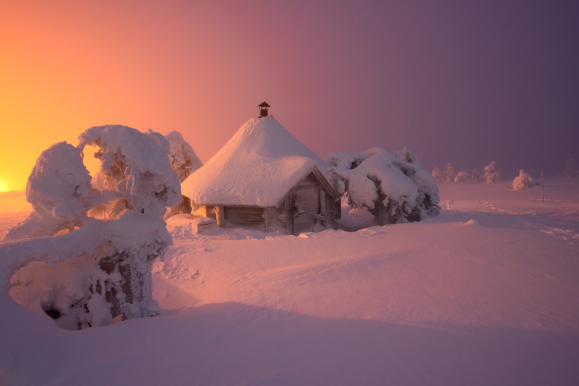 HD PC desktop wallpaper: snow-covered man-made hut and frosted trees bathed in warm sunset light in a quiet winter landscape.
