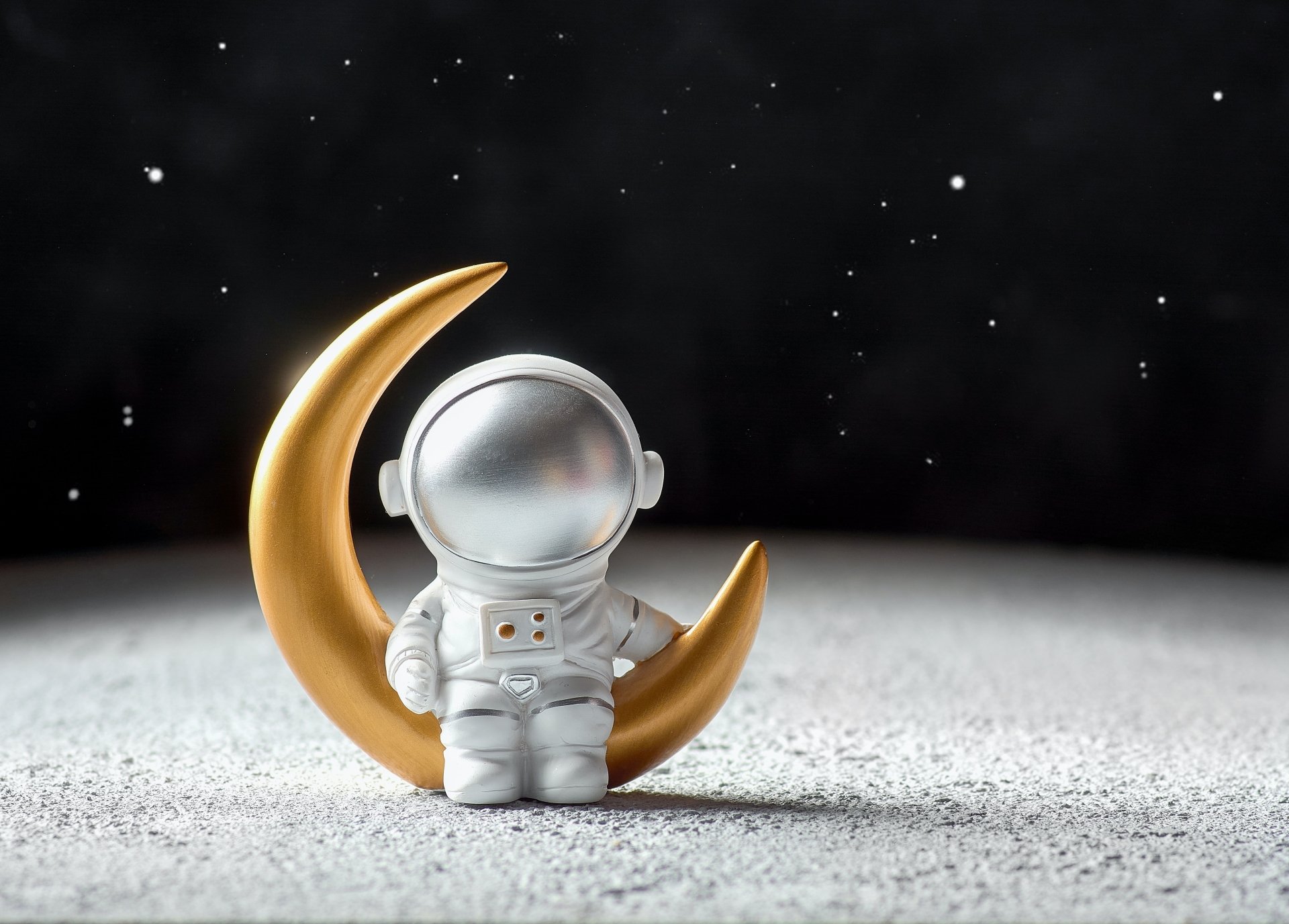 A 4K Ultra HD sci-fi desktop wallpaper of a small astronaut figure standing next to a golden crescent moon against a dark, starry space background.