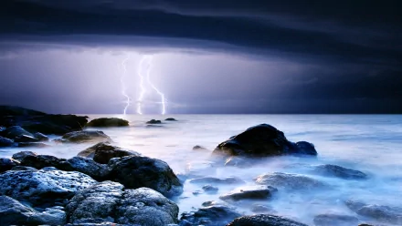 HD desktop wallpaper showing a stormy ocean scene with dark clouds, lightning striking over the water, and rocky shore in the foreground, highlighting dramatic natural power.