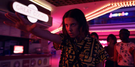 HD PC desktop wallpaper of Stranger Things' Eleven — intense teen with a focused, telekinetic stare and outstretched hand in a neon-lit arcade.