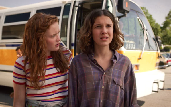 HD PC wallpaper of Max Mayfield and Eleven from the TV show Stranger Things standing by a yellow school bus, both looking concerned.