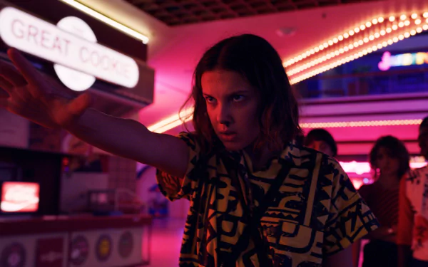 HD PC desktop wallpaper of Stranger Things' Eleven — intense teen with a focused, telekinetic stare and outstretched hand in a neon-lit arcade.