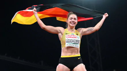 HD desktop wallpaper of a German athlete — a smiling sprinter holding the German flag overhead in a stadium celebration after a race win.