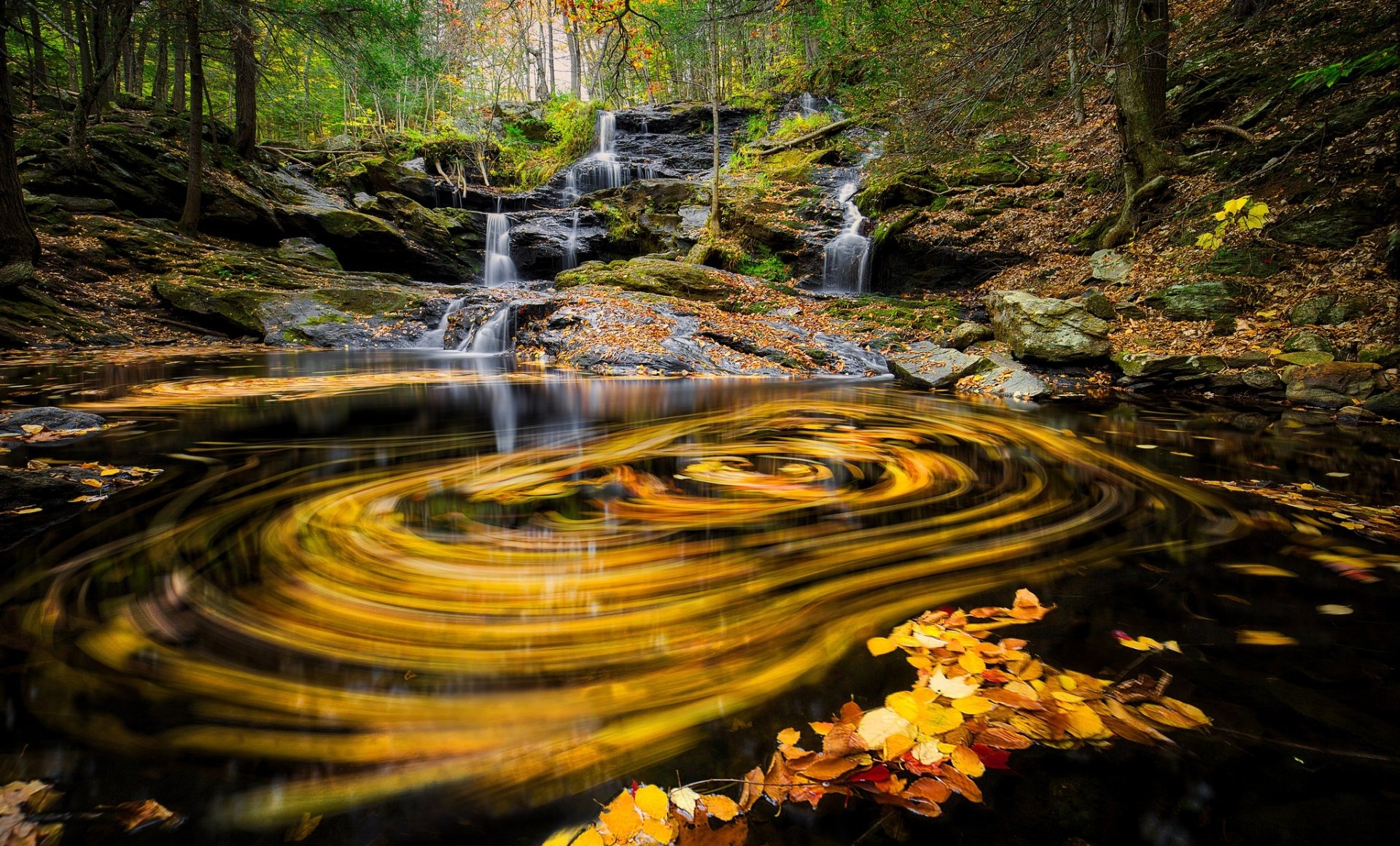 HD PC desktop wallpaper and background: a forest nature scene with a multi-tiered waterfall flowing into a swirling pool of autumn leaves.