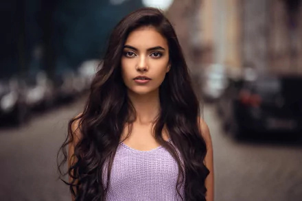 HD desktop wallpaper featuring a confident woman model with long dark hair, wearing a lavender top, standing outdoors on a blurred street background.
