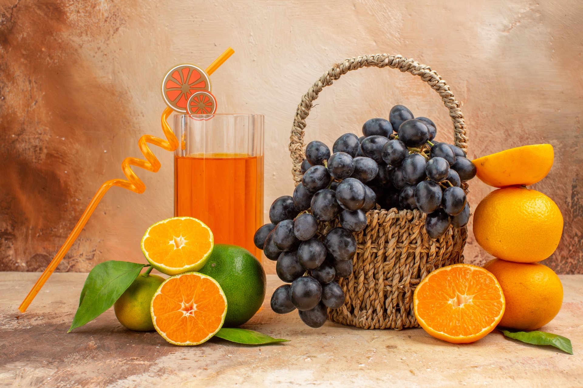 A vibrant 4K Ultra HD desktop wallpaper featuring fresh fruit including black grapes in a basket, bright oranges, green citrus, and a glass of orange juice with a straw.