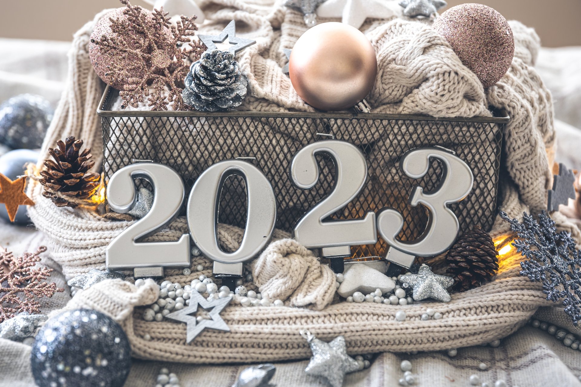 Cozy holiday scene with knitted fabric, ornaments, pinecones, and wooden numbers forming 2023, designed as a 4K Ultra HD New Year 2023 PC desktop wallpaper.