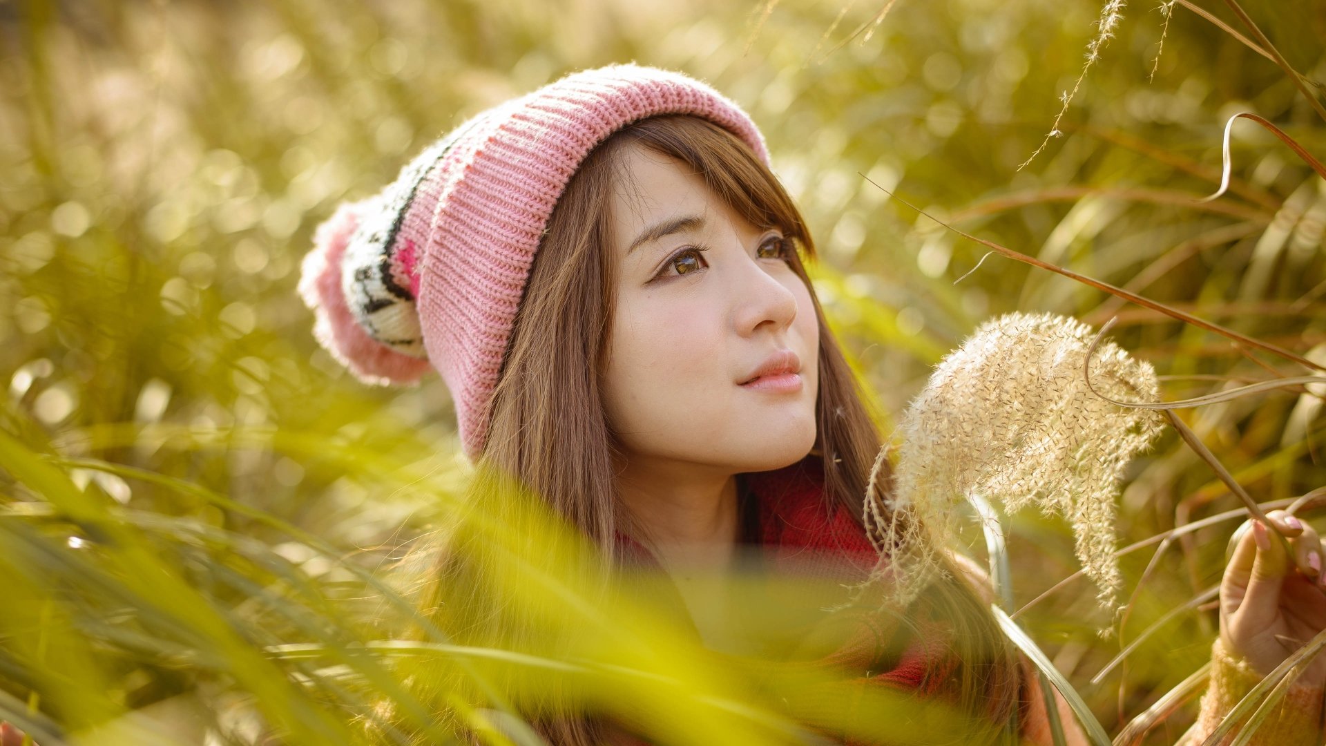 A 4K Ultra HD image of an Asian woman wearing a pink knit hat, surrounded by golden foliage in a serene outdoor setting.
