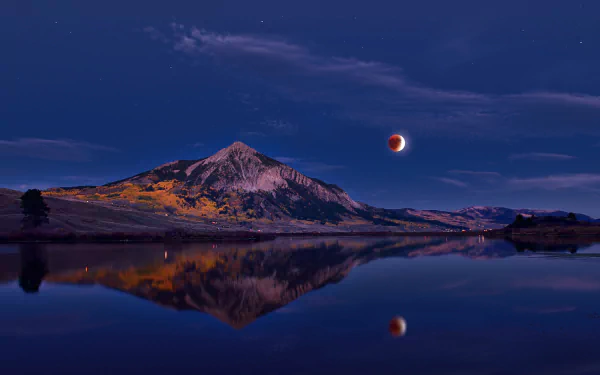 Majestic mountain under lunar eclipse with full moon reflecting in calm water, a captivating HD desktop wallpaper.
