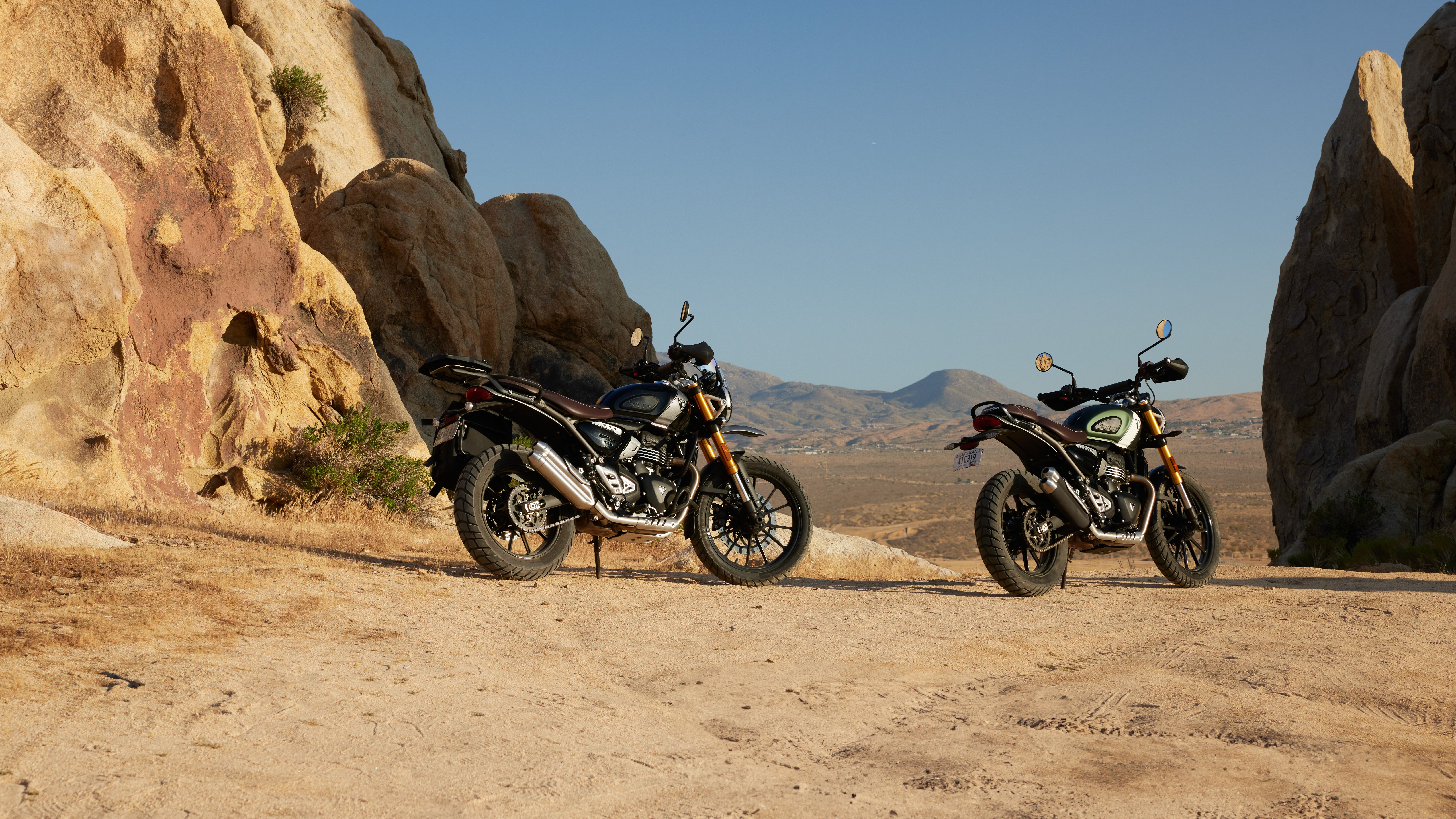 HD wallpaper of Triumph Speed 400 and Triumph Scrambler 400 X motorcycles parked side by side in a scenic desert landscape, ideal for a desktop background.