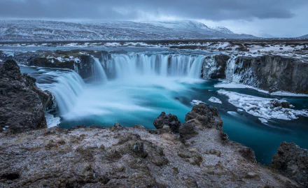 HD desktop wallpaper showcasing Goðafoss waterfall in Iceland, capturing the serene beauty of nature with flowing turquoise waters and rugged rocky surroundings.