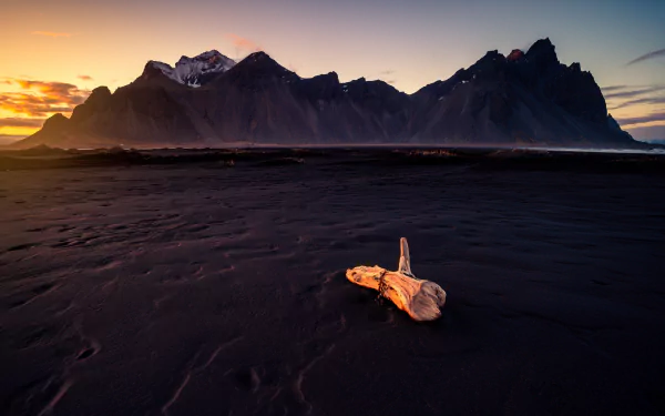 Nature 5K Ultra HD PC desktop wallpaper of Vestrahorn: sunrise over jagged peaks, black sand beach with driftwood in foreground and low coastal mist under a warm sky.
