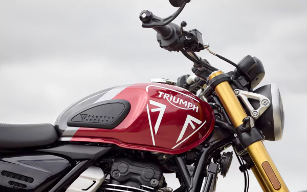 HD wallpaper featuring a close-up of a Triumph Speed Triple 1200 RR's tank and handlebars against a cloudy sky.