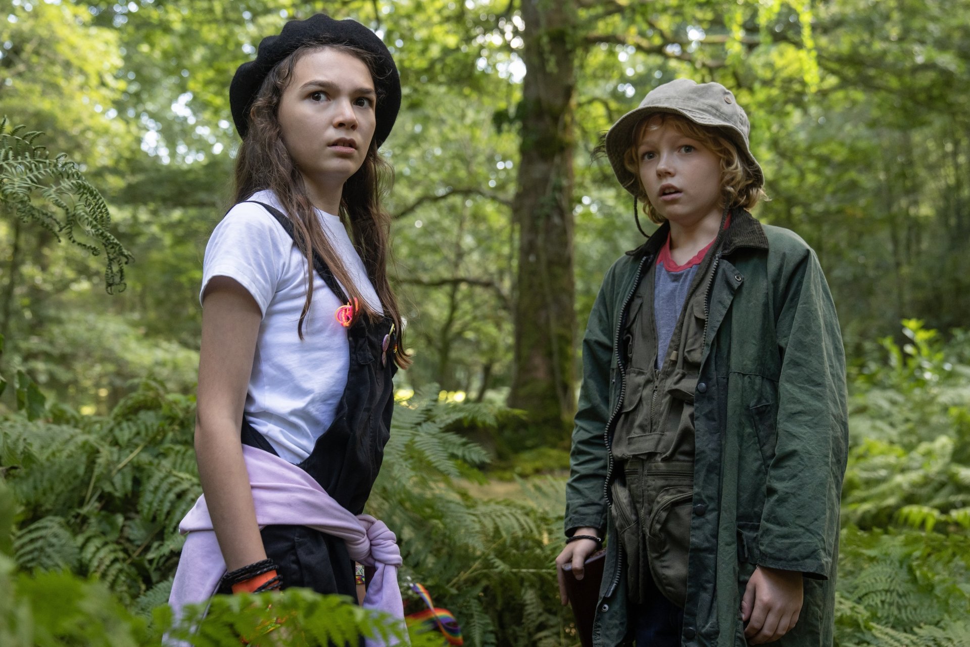 Two children looking alert in a forest setting, potentially a scene from the Cocaine Bear movie, available as a high-definition desktop wallpaper and background.