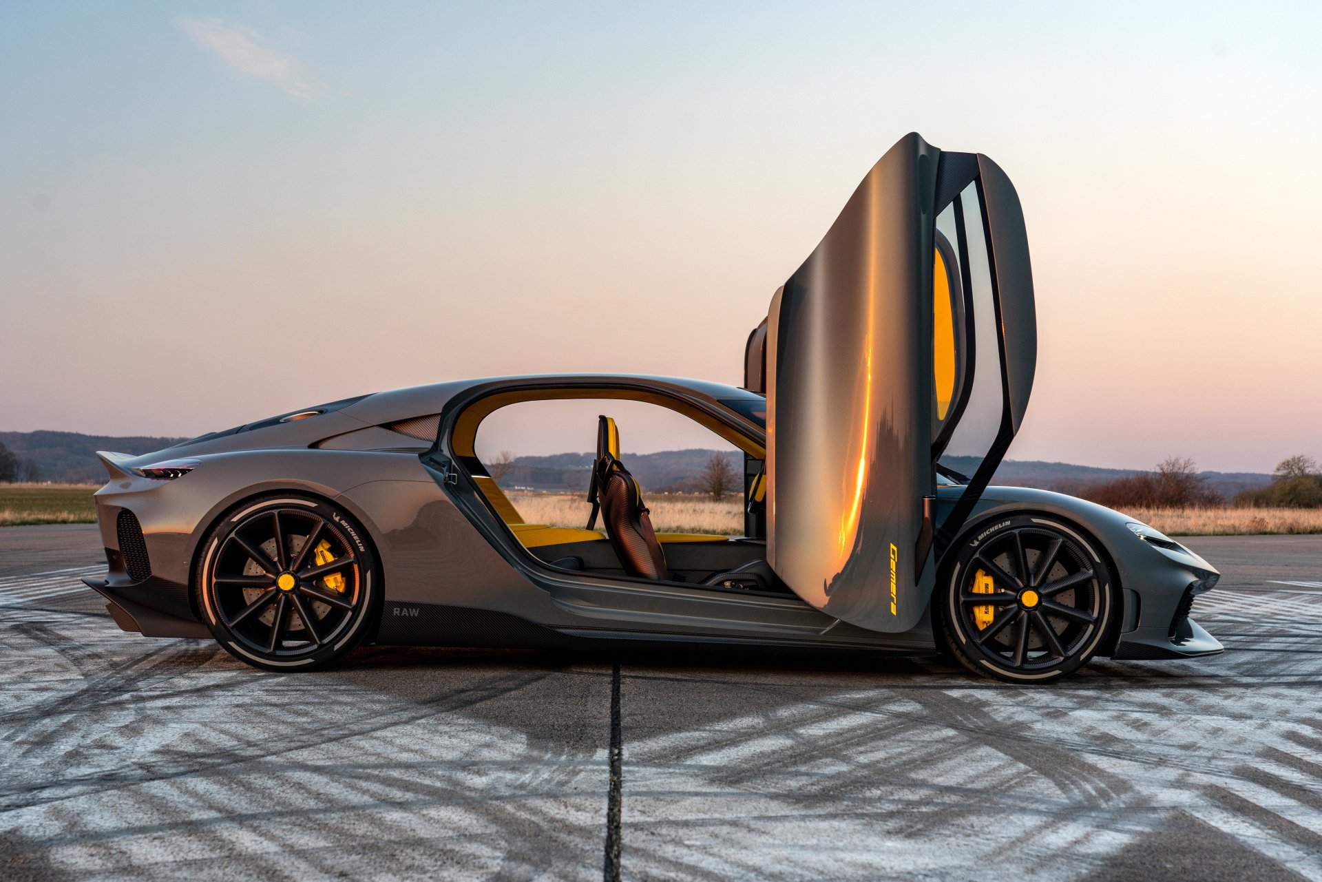 A stunning Koenigsegg Gemera with its distinctive doors open, showcased against a serene sunset backdrop. This HD wallpaper captures the car's sleek design and dynamic presence.